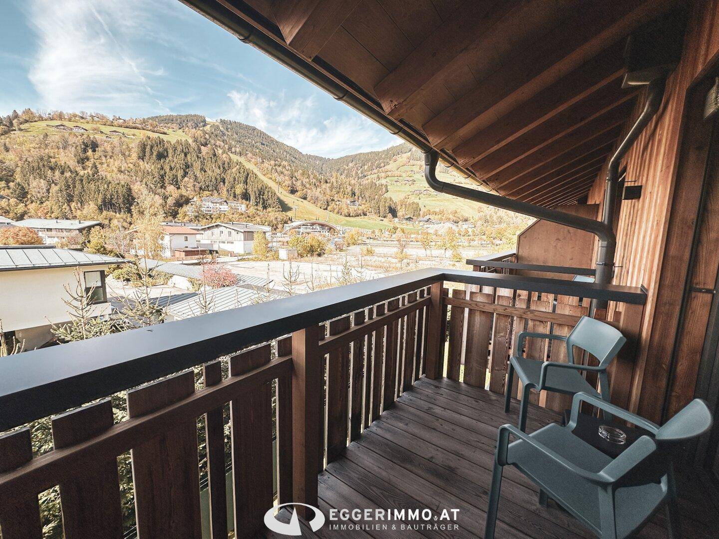 Geräumiger Holzbalkon mit Sitzgelegenheiten und weitem Blick auf die umliegende Berglandschaft.