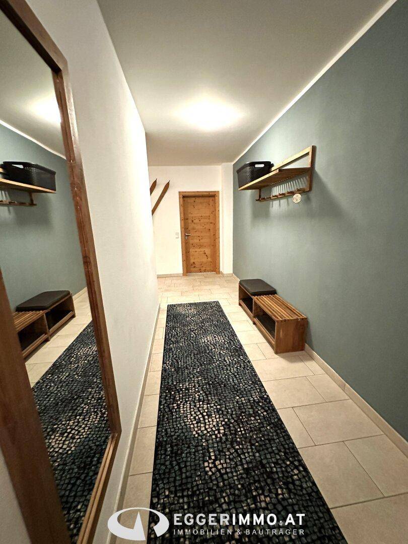 Heller Eingangsbereich mit Fliesenboden, großem Spiegel, Holzbänken und Garderobe, ideal für Skiausrüstung.