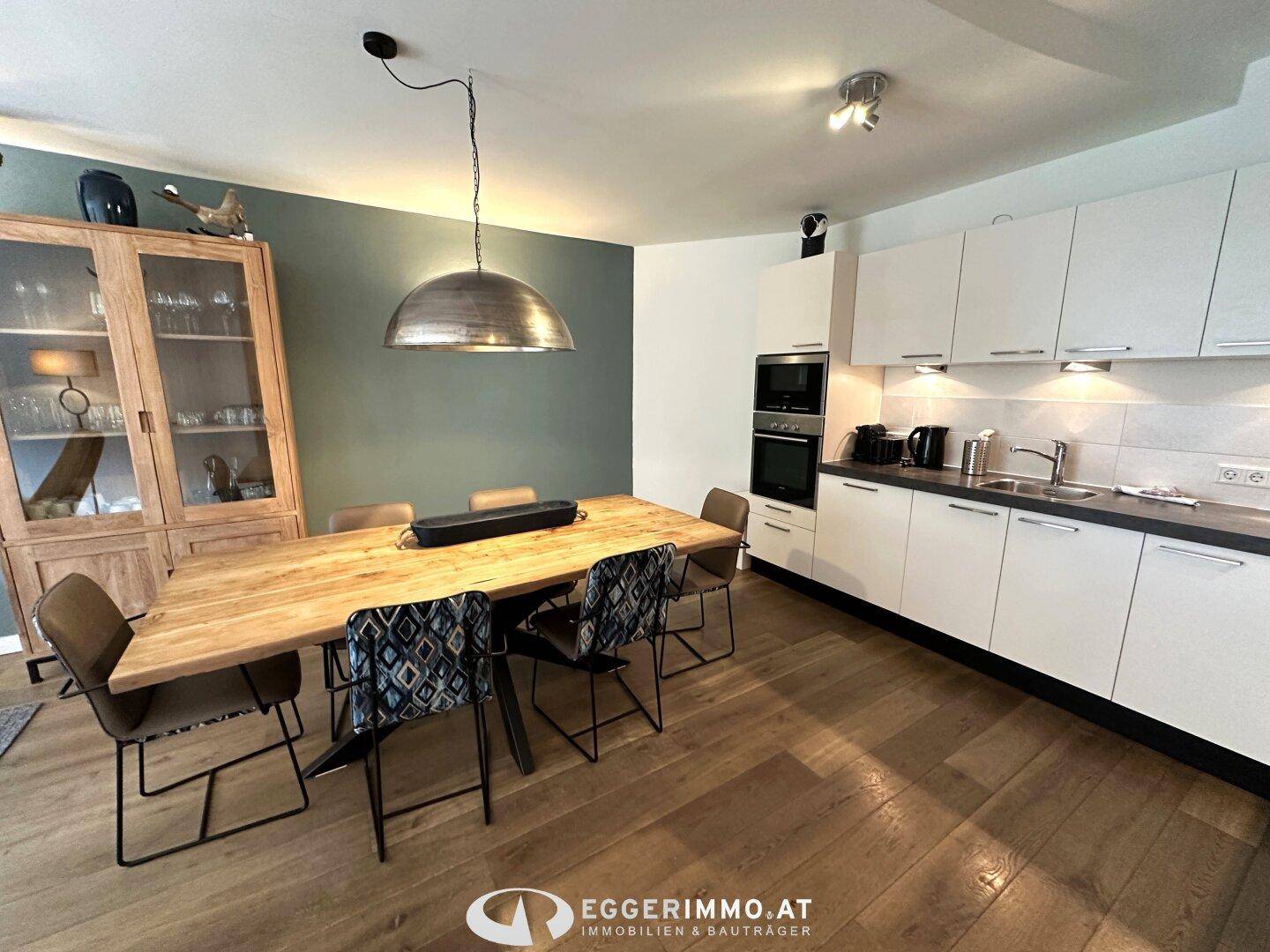 Moderne Küche mit weißen Schränken, integrierten Geräten und großem Holzesstisch, perfekt für gesellige Runden.