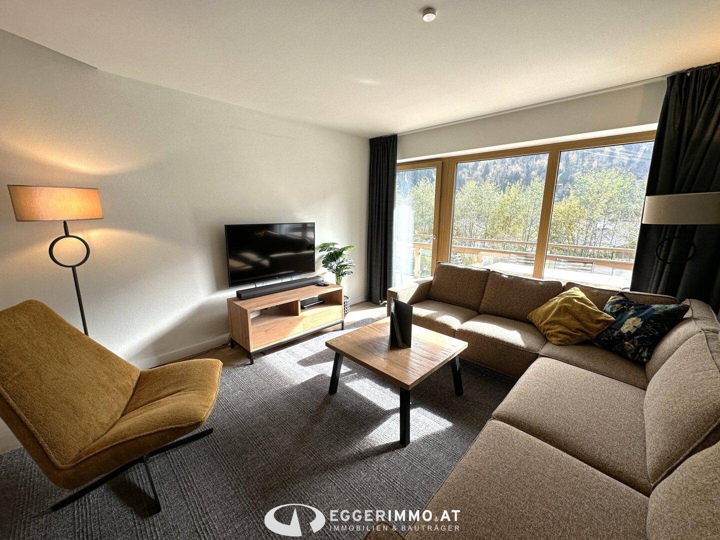 Gemütlicher Wohnbereich mit Ecksofa, Fernseher und großen Fenstern, die einen schönen Blick auf die Berge bieten.