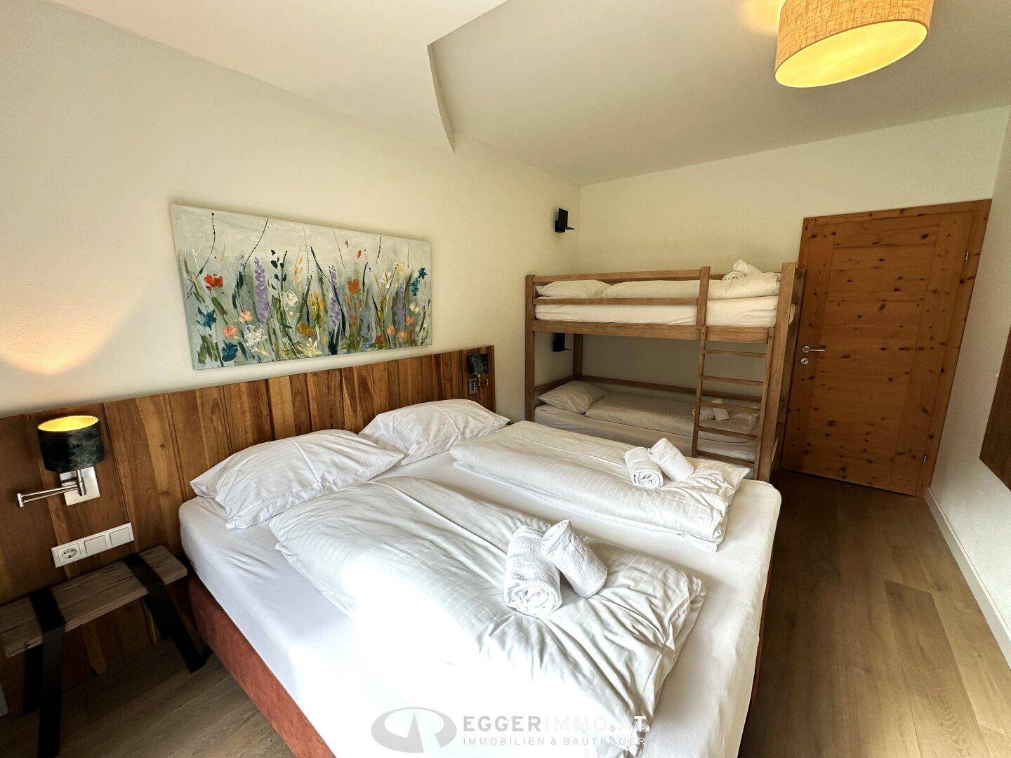 Schlafzimmer mit Doppelbett, Etagenbett und Kunstwerk an der Wand, das eine freundliche Atmosphäre schafft.