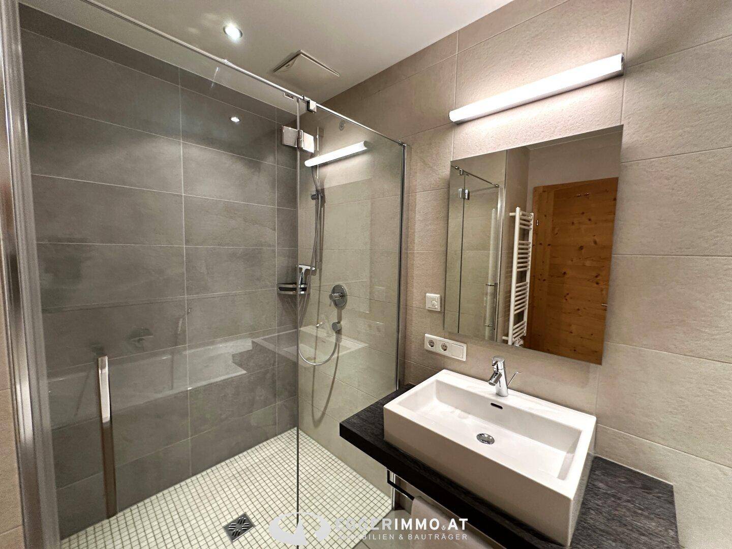 Modernes Badezimmer mit begehbarer Dusche, Waschbecken und grauen Fliesen, sehr stilvoll und funktional.