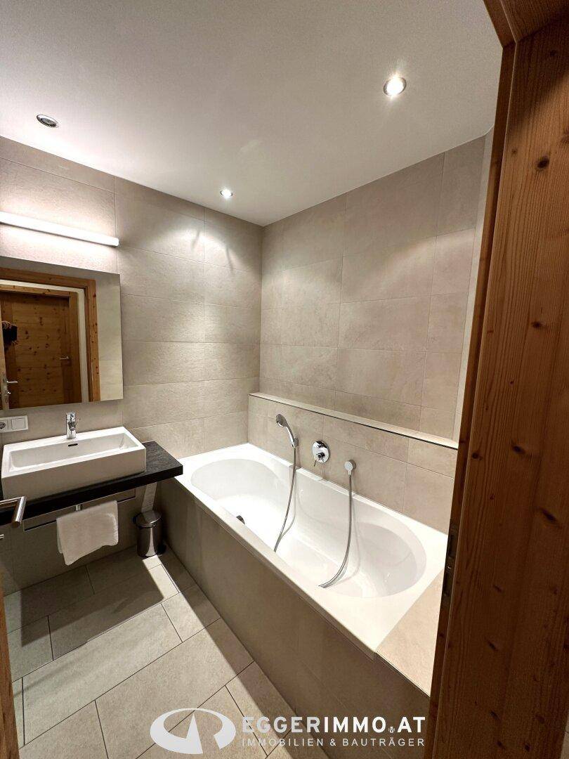 Modernes Badezimmer mit Badewanne, Waschbecken und hellen Fliesen, bietet Komfort und Entspannung.