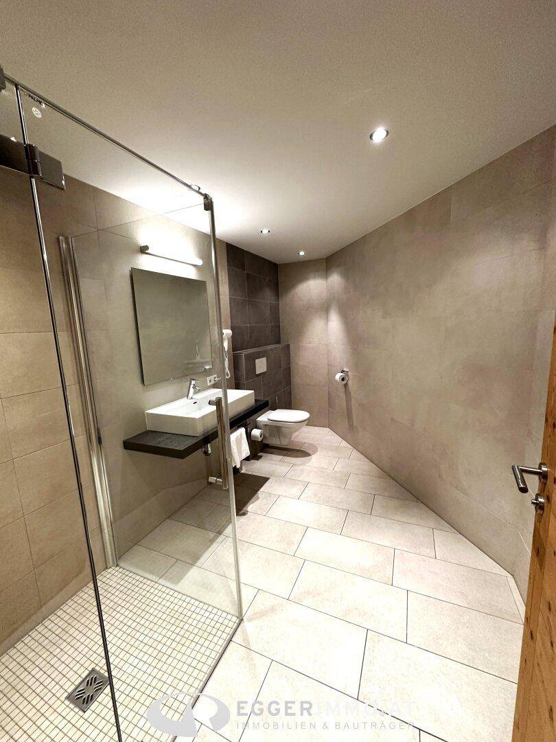 Modernes Badezimmer mit Duschkabine, wandhängendem WC und hellen Fliesen, sehr sauber und zeitgemäß.
