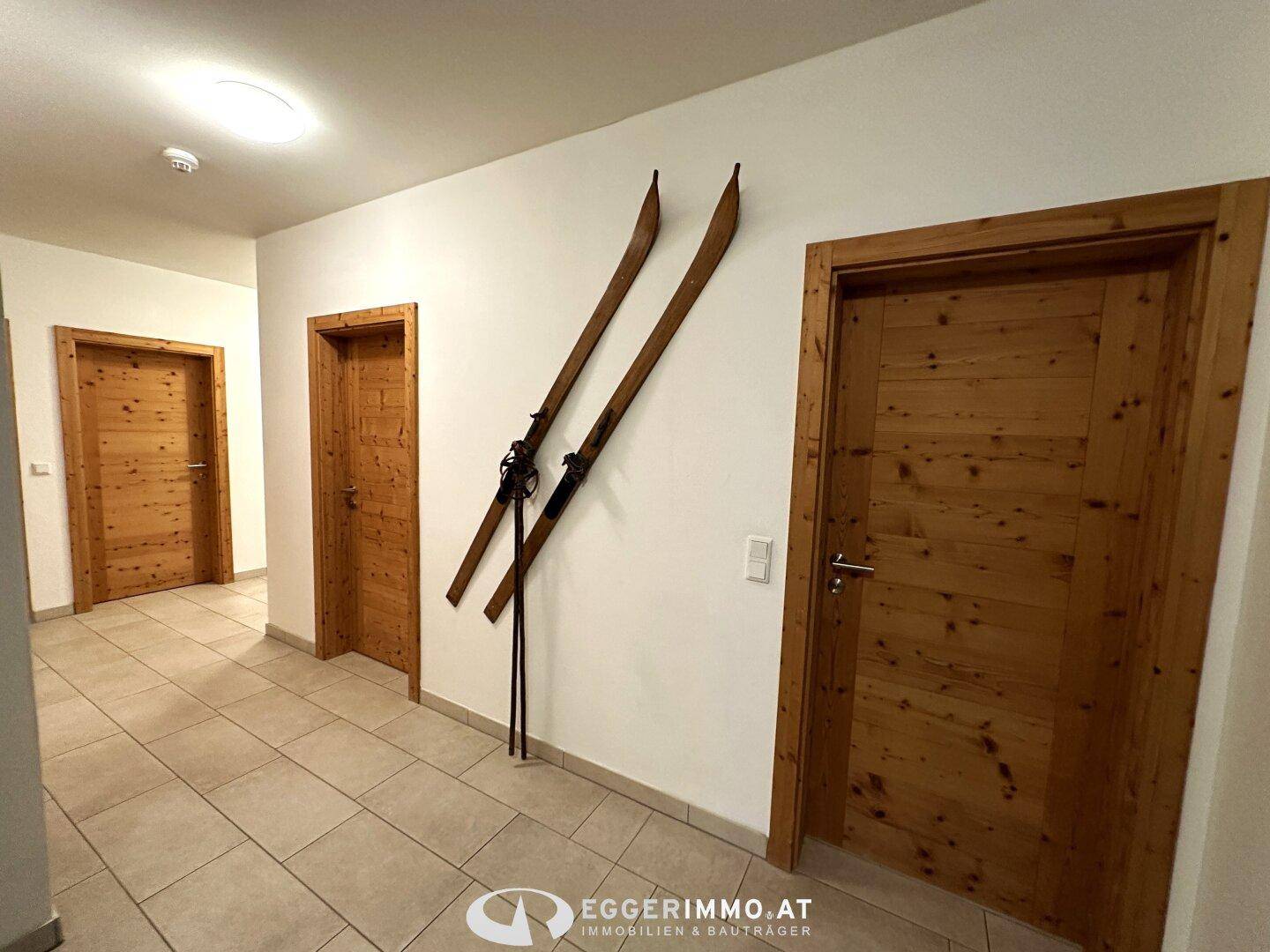 Flur mit hellen Fliesen, Holztüren und dekorativen Skiern an der Wand, die einen alpinen Charme verleihen.