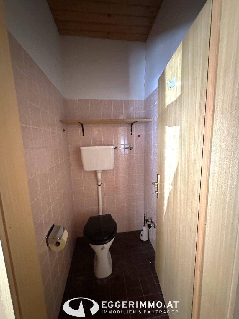Toilettenraum mit rosa Fliesen, Holzdecke und einer Toilette mit dunklem Sitz.