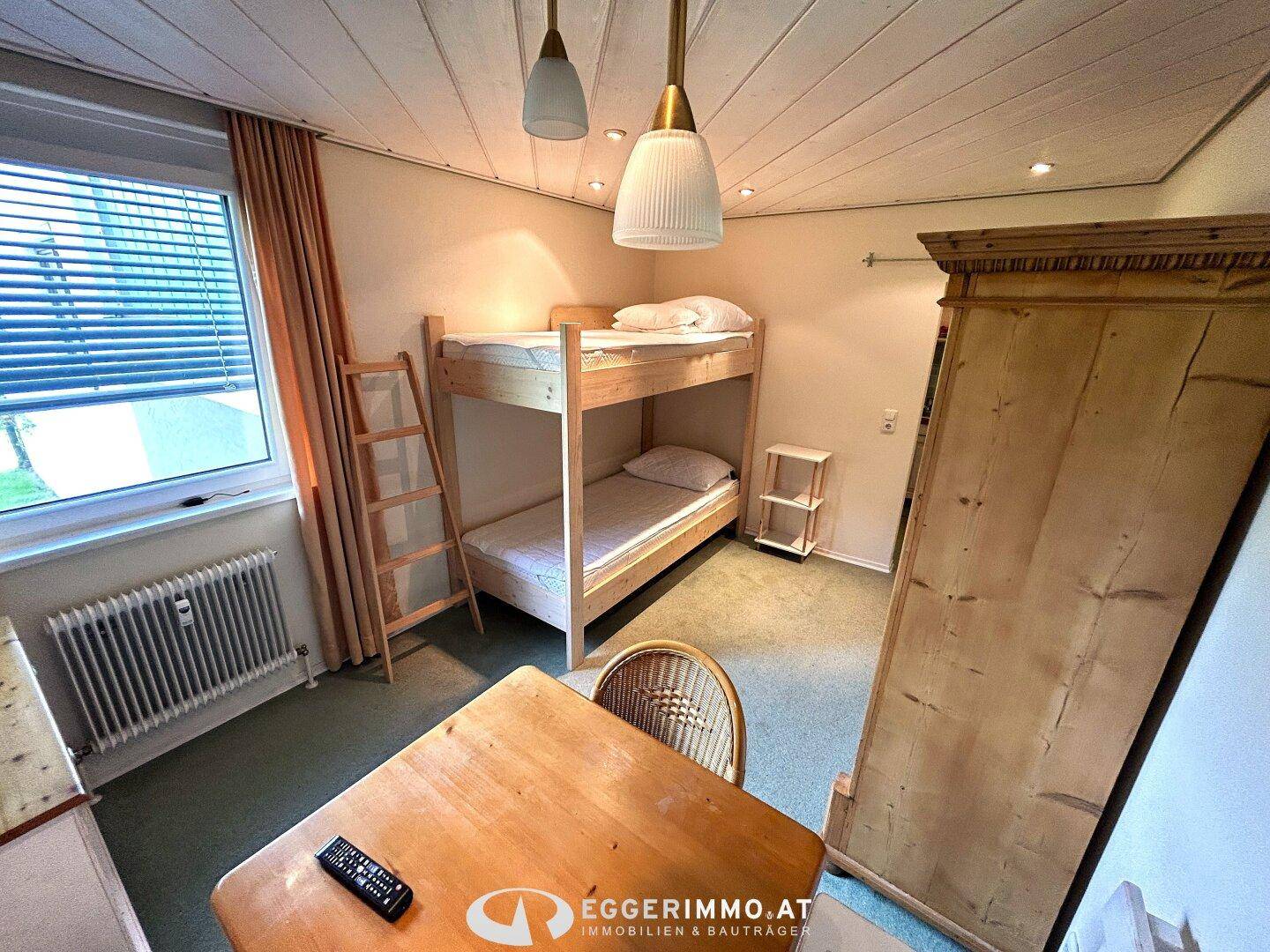 Helles Schlafzimmer mit Etagenbett, Holzmöbeln und Fenster, das Tageslicht hereinlässt.