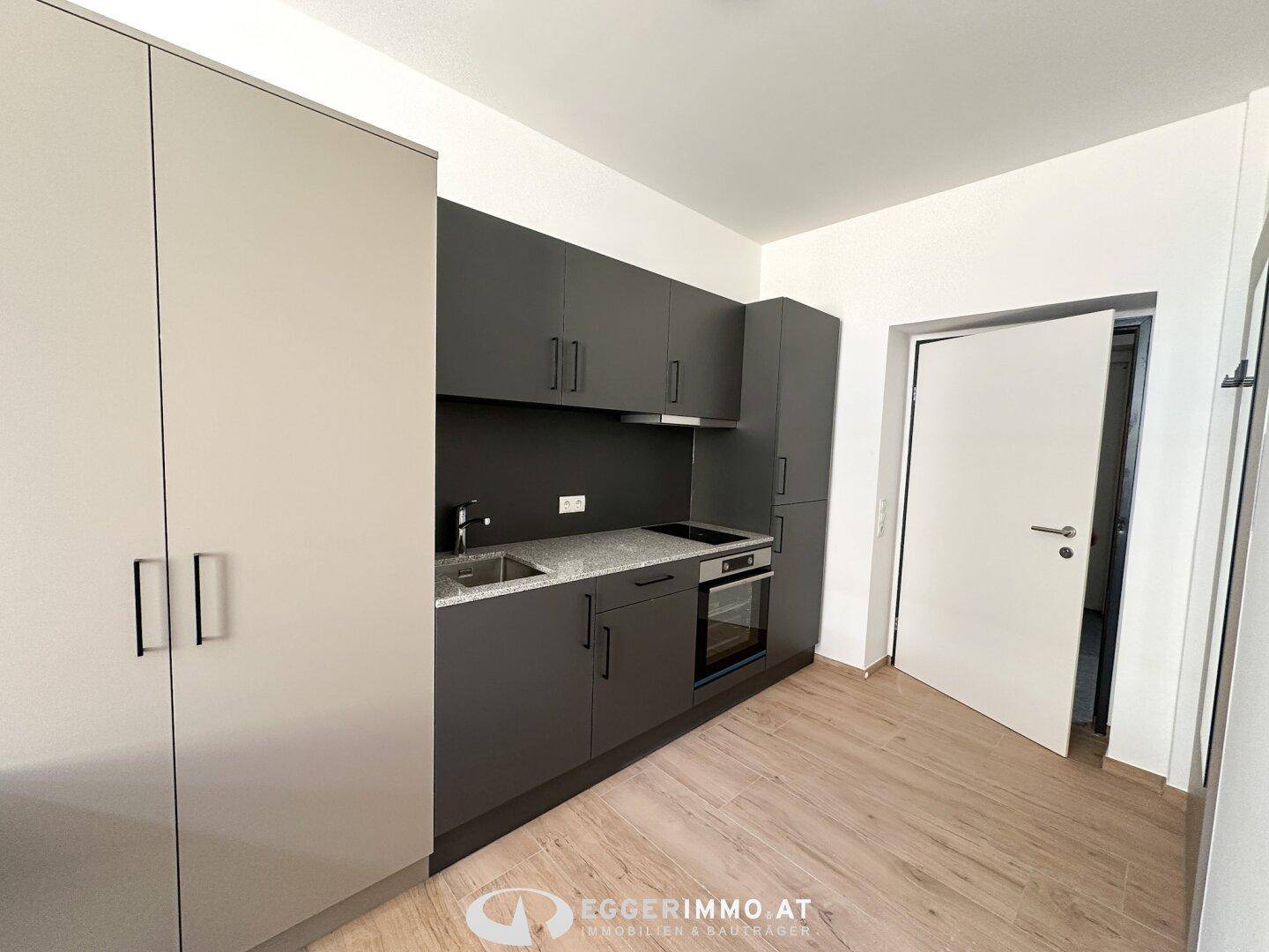 Moderne Küchenzeile mit grauen Schränken, integriertem Backofen und hellem Laminatboden.