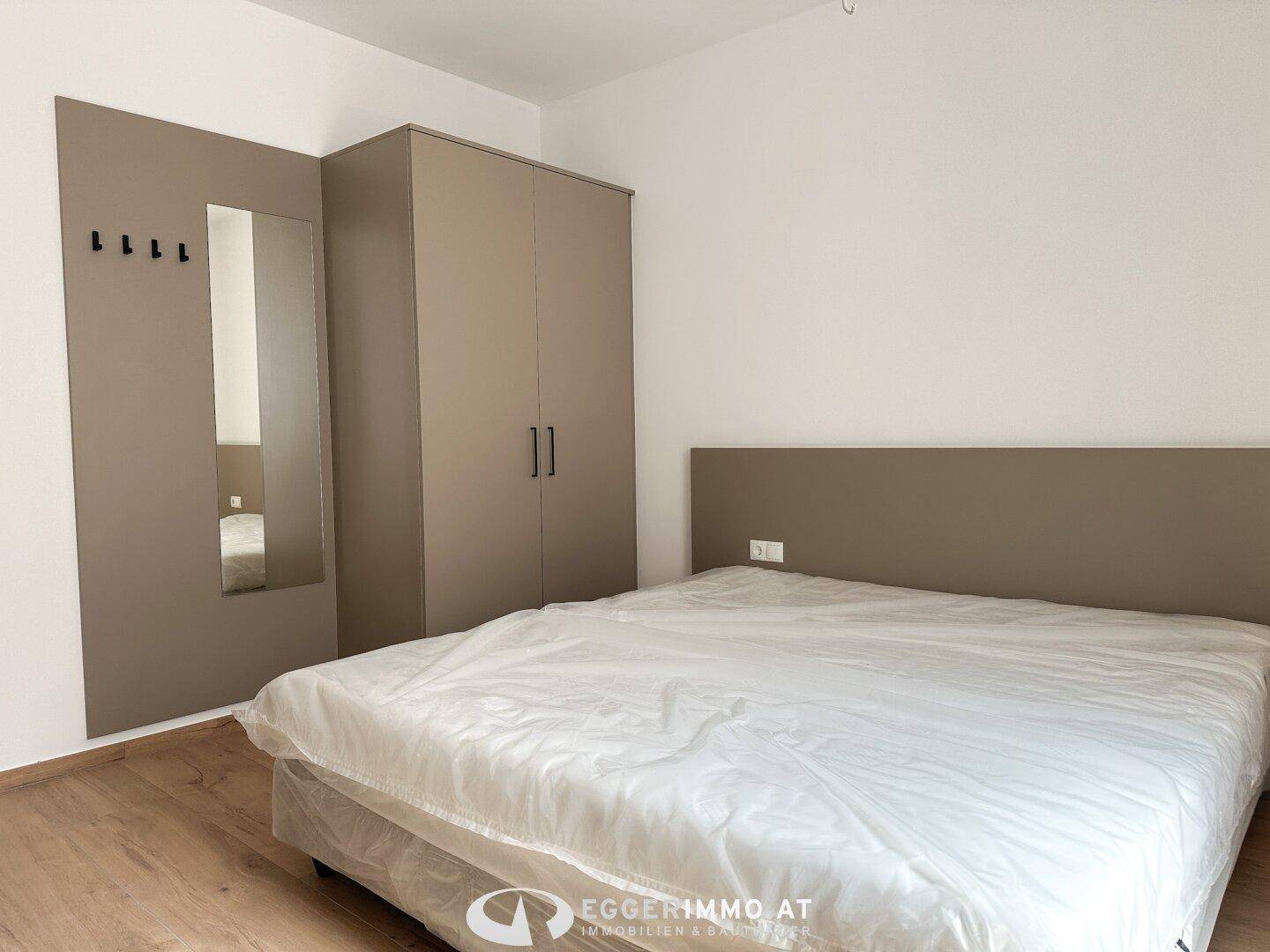 Helles Schlafzimmer mit modernem Kleiderschrank, Bett und integriertem Spiegel.