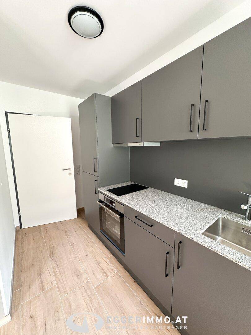 Kompakte Küchenzeile mit grauen Schränken, Granit-Arbeitsplatte und modernen Geräten.