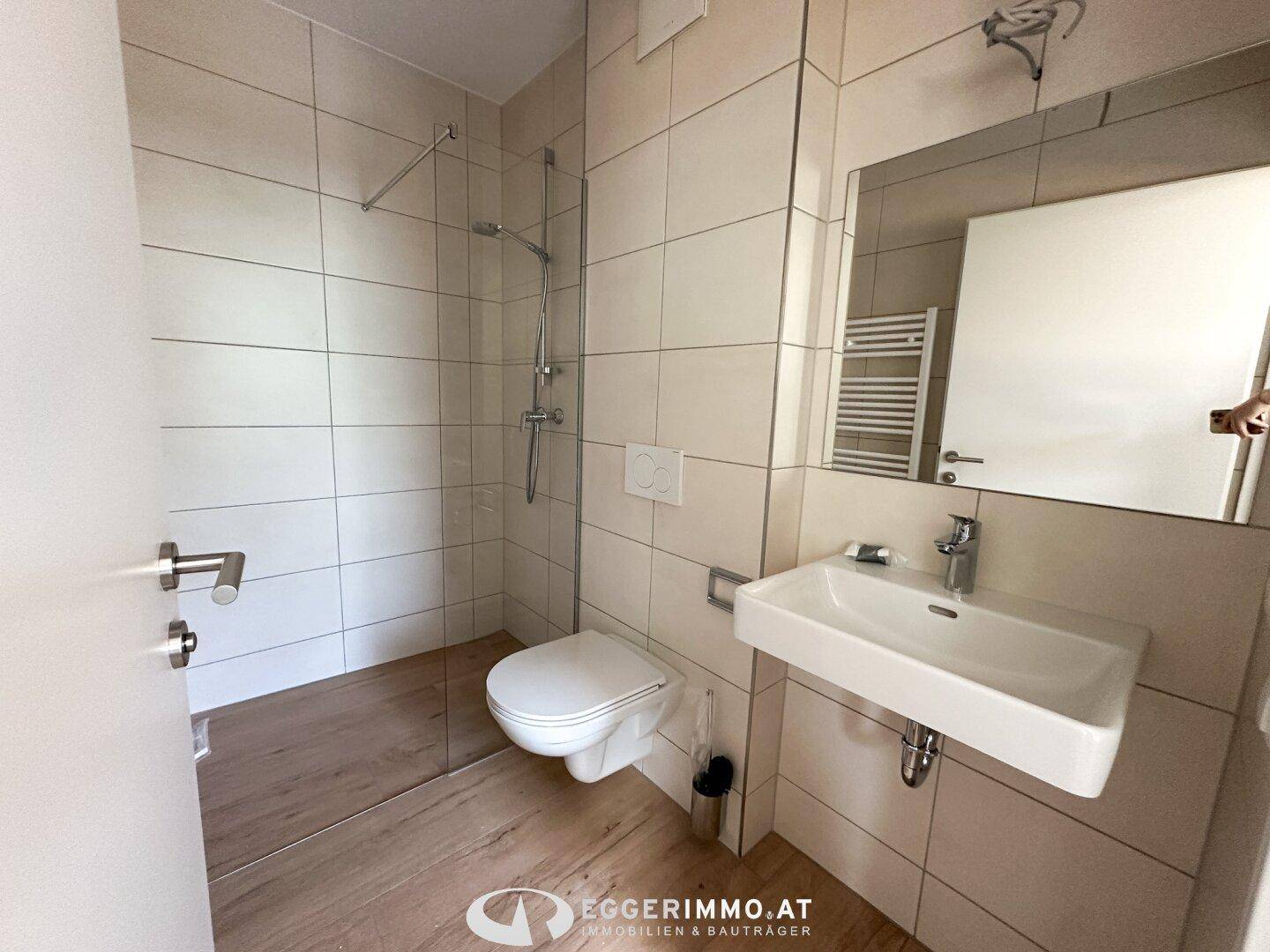 Helles Badezimmer mit ebenerdiger Dusche, Wand-WC, Waschbecken und beheiztem Handtuchhalter.