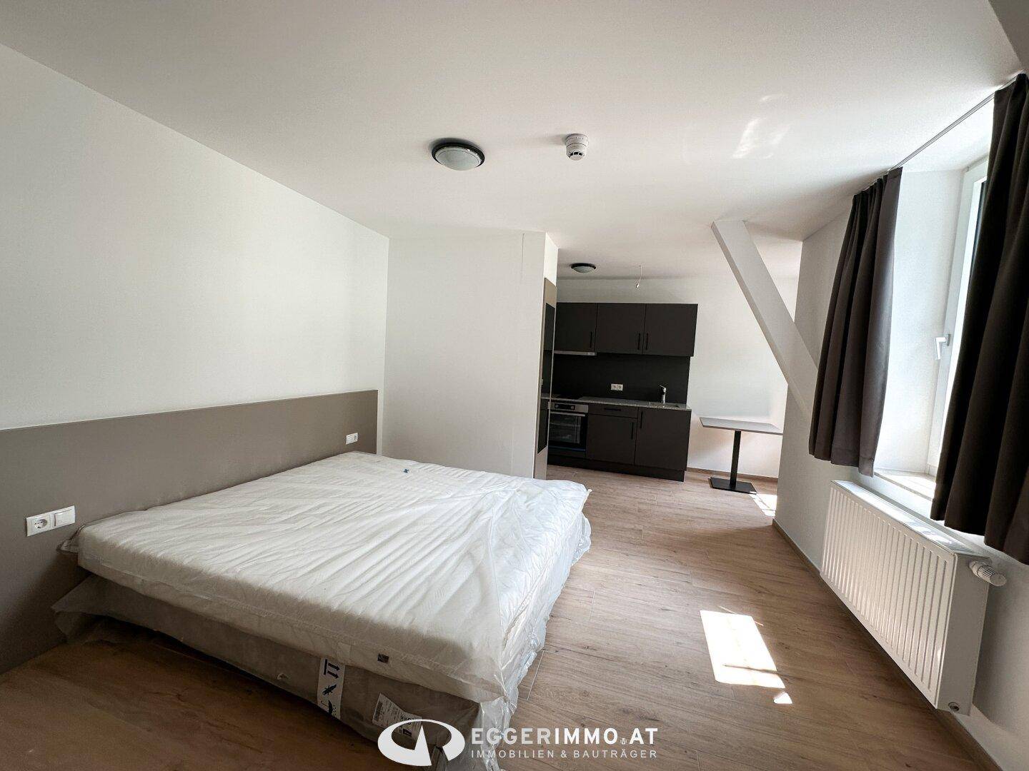 Studio-Apartment mit Schlafbereich, integrierter Küchenzeile und kleinem Esstisch.