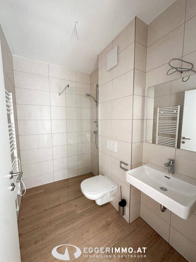 Helles Badezimmer mit ebenerdiger Dusche, modernem Waschbecken und WC.