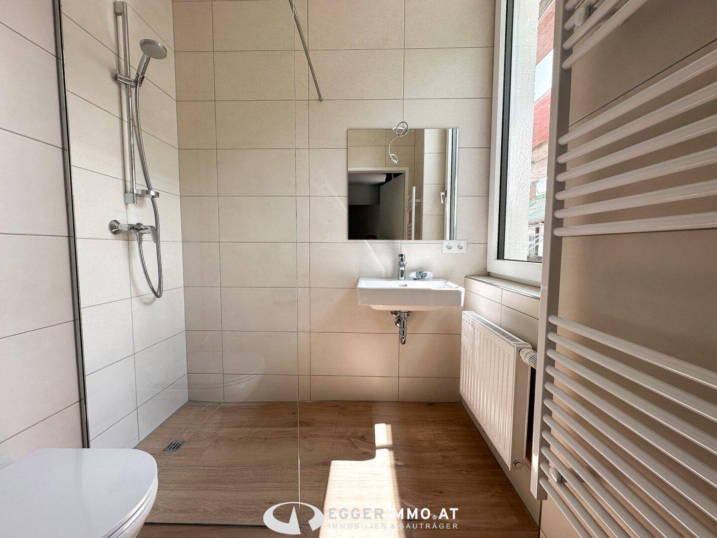 Helles Badezimmer mit begehbarer Dusche, Wand-WC, Waschbecken und einem Fenster für Tageslicht.
