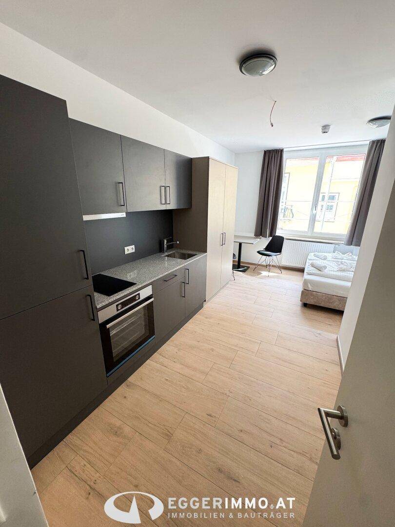 Moderne Küchenzeile mit Backofen und angrenzendem Schlafbereich mit Fenster.