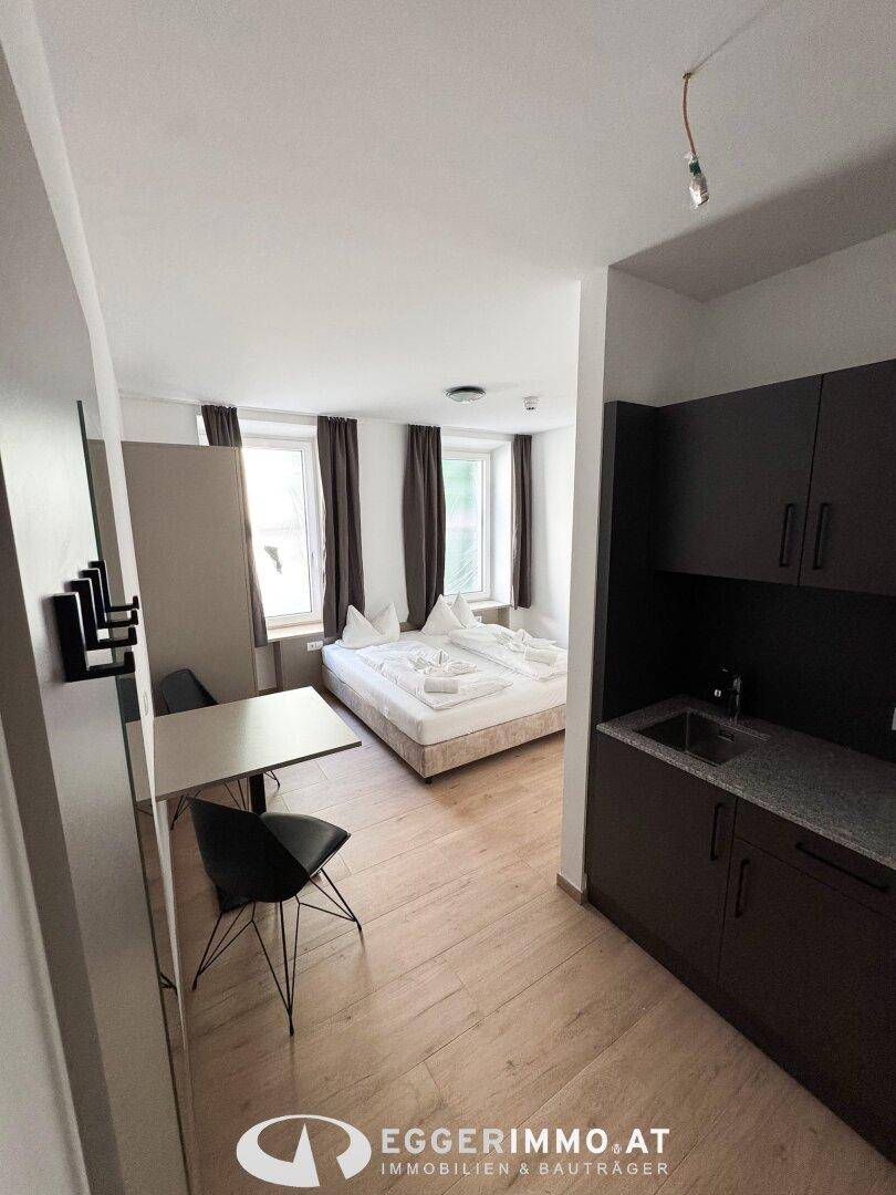 Helles Schlafzimmer mit integrierter Küchenzeile und Holzboden in modernem Stil.