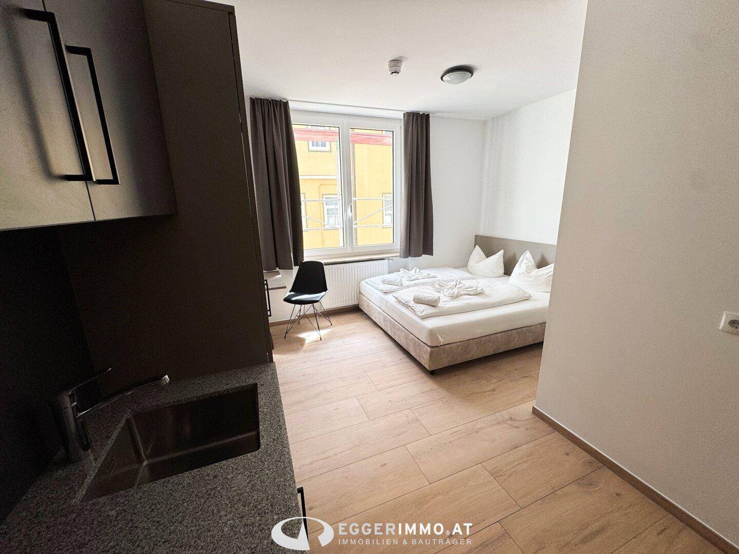 Schlafzimmer mit integrierter Küchenzeile und Blick aus dem Fenster.