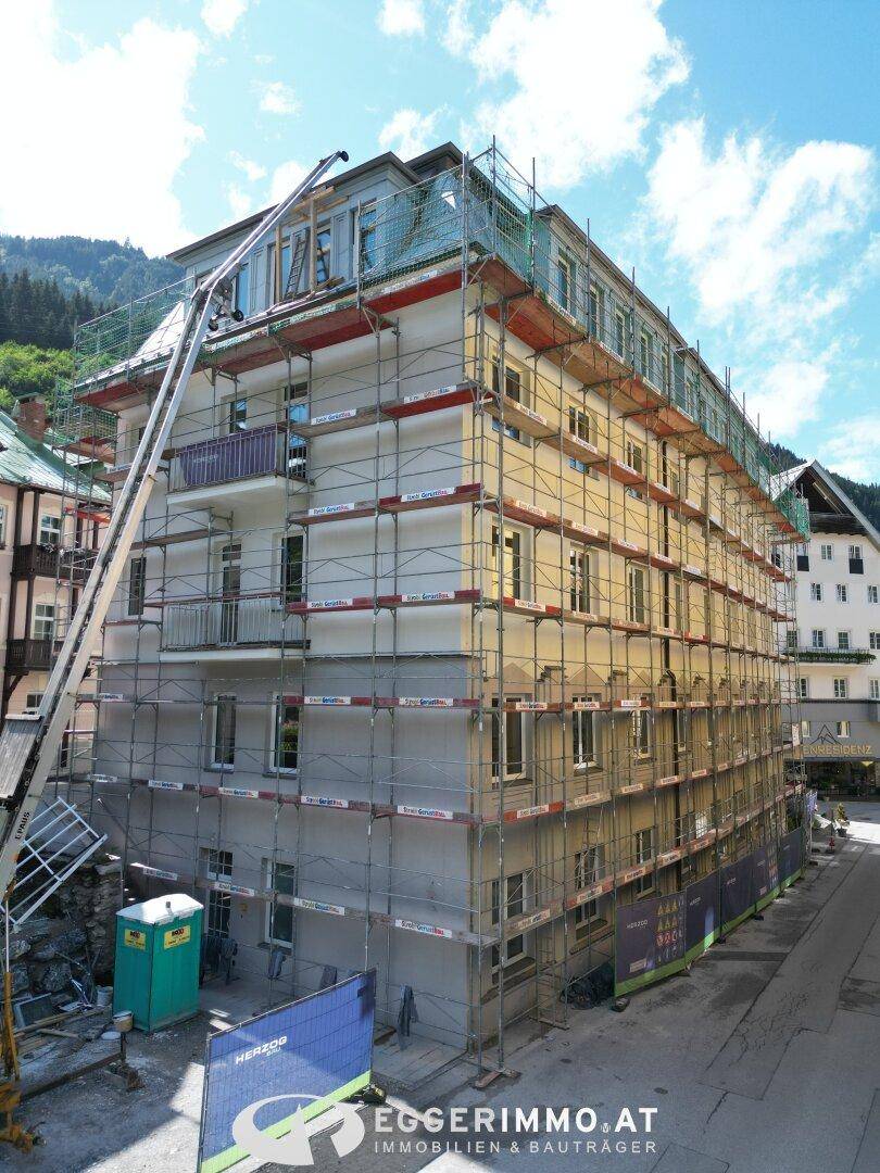 Fassade eines Gebäudes in Renovierung mit Gerüsten und Bergblick unter blauem Himmel.