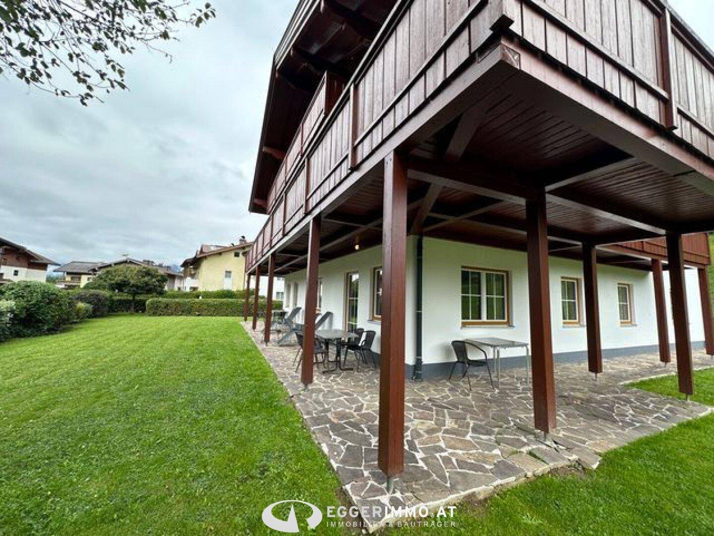 Geräumige überdachte Terrasse mit Sitzgelegenheiten und großem Gartenbereich, umgeben von grüner Landschaft.