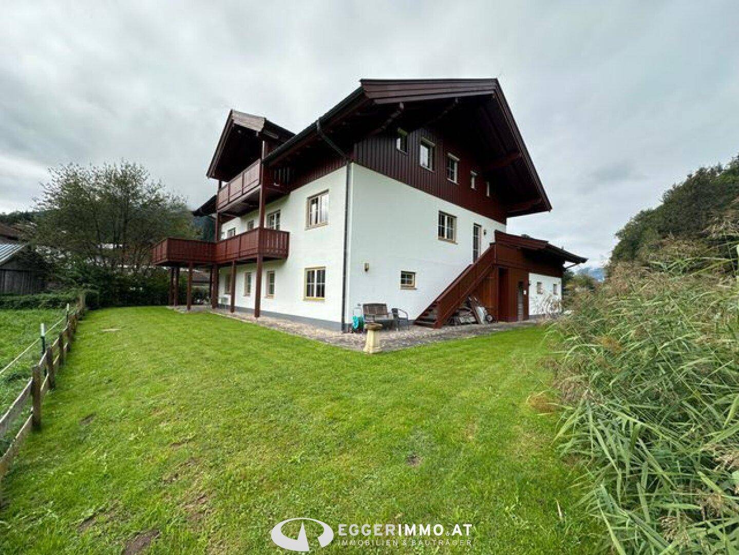 Traditionelles Haus mit Holzfassade und mehreren Balkonen, eingebettet in eine grüne Umgebung.