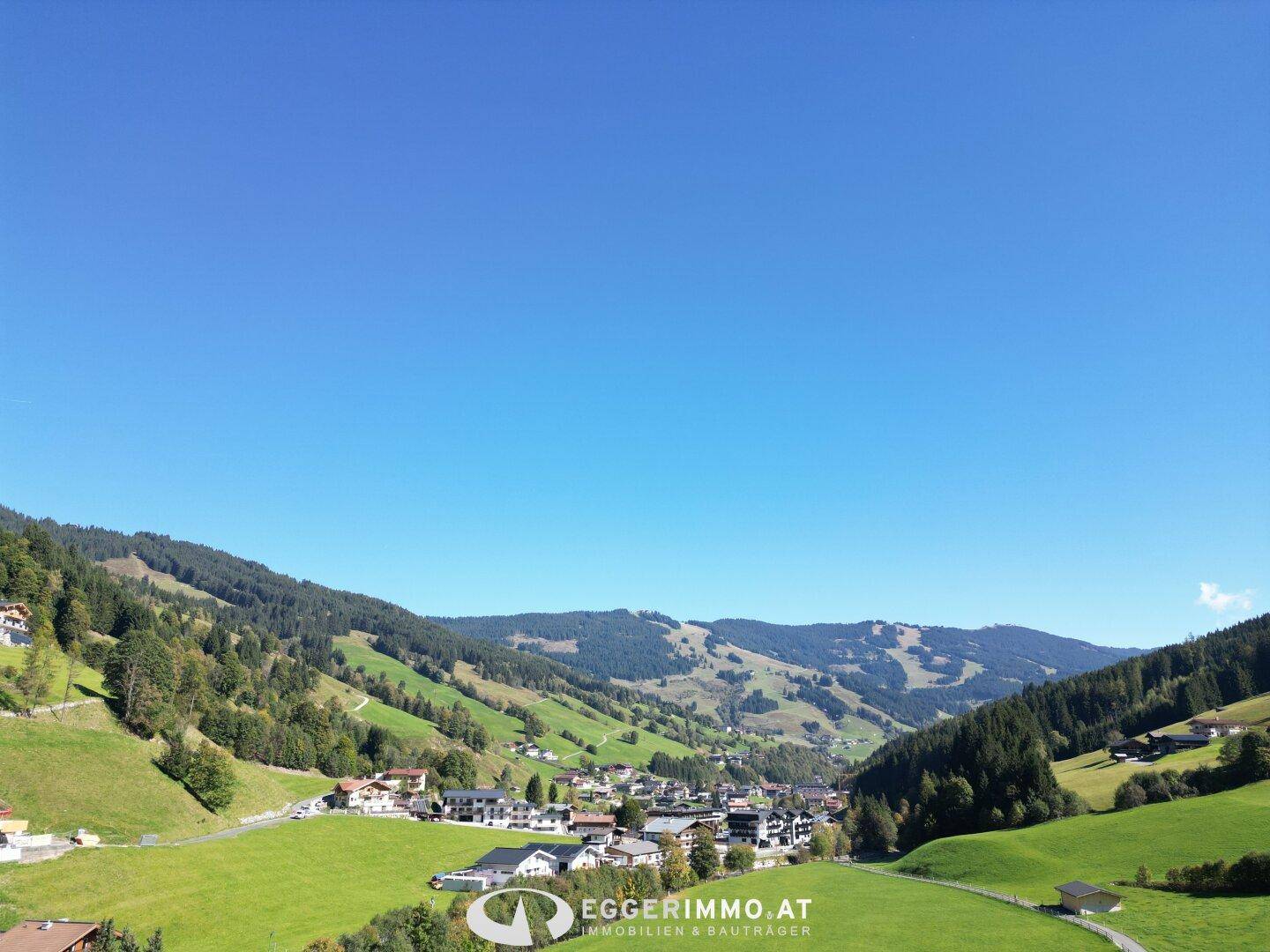 Weitläufiger Blick über ein grünes Tal mit verstreuten Häusern und majestätischen Bergen am Horizont.