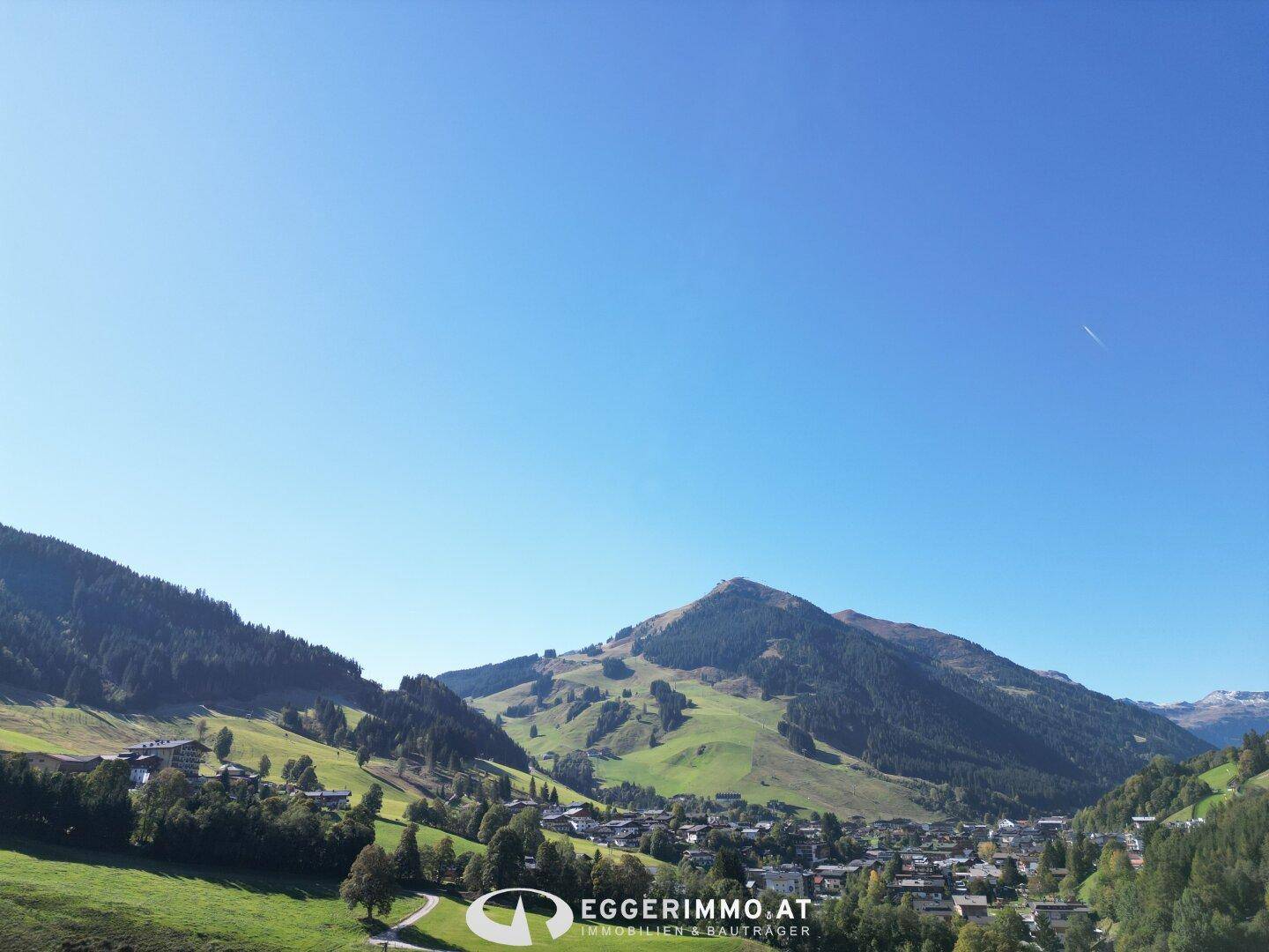 Panoramablick auf eine idyllische Berglandschaft mit einem kleinen Dorf im Tal unter blauem Himmel.