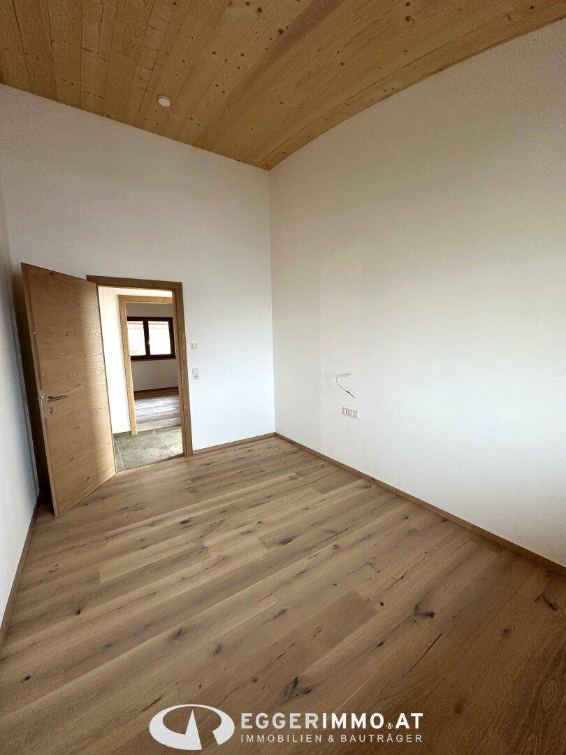 Helles Zimmer mit Holzboden, Holzdecke und einer Holztür, bereit zur individuellen Gestaltung.