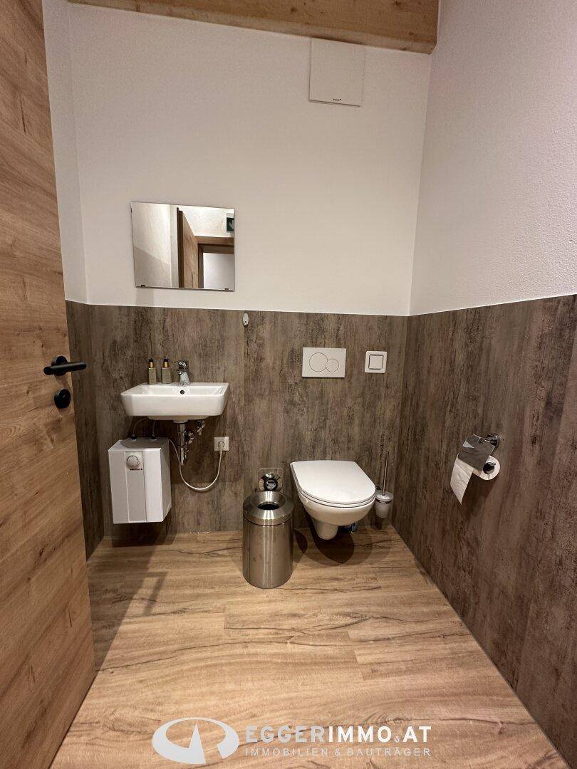 Modernes Gäste-WC mit Wand-WC, kleinem Waschbecken und Holzoptik-Verkleidung an den Wänden und Vinylboden.