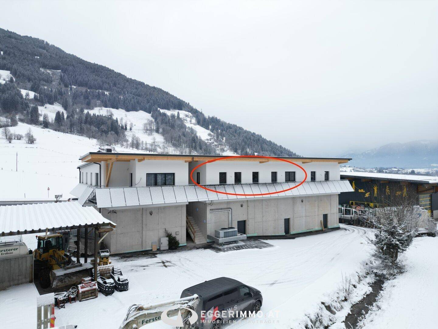 Modernes Gebäude mit Flachdach und einer Reihe von Fenstern im Obergeschoss, umgeben von Schnee und Bergen.