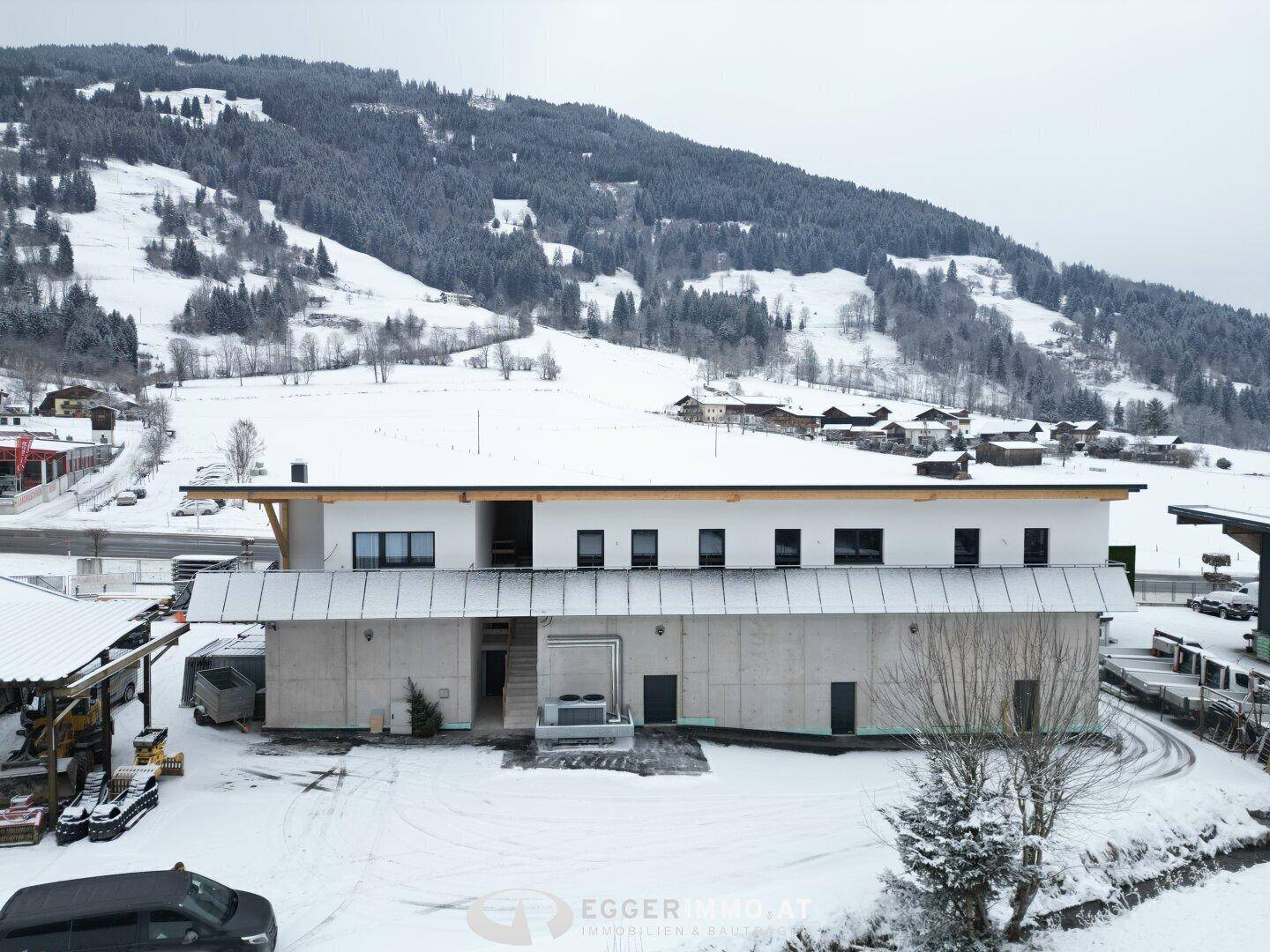 Seitenansicht des modernen Gebäudes im Winter, mit verschneiten Hängen und Bergen im Hintergrund, die die ländliche Umgebung zeigen.