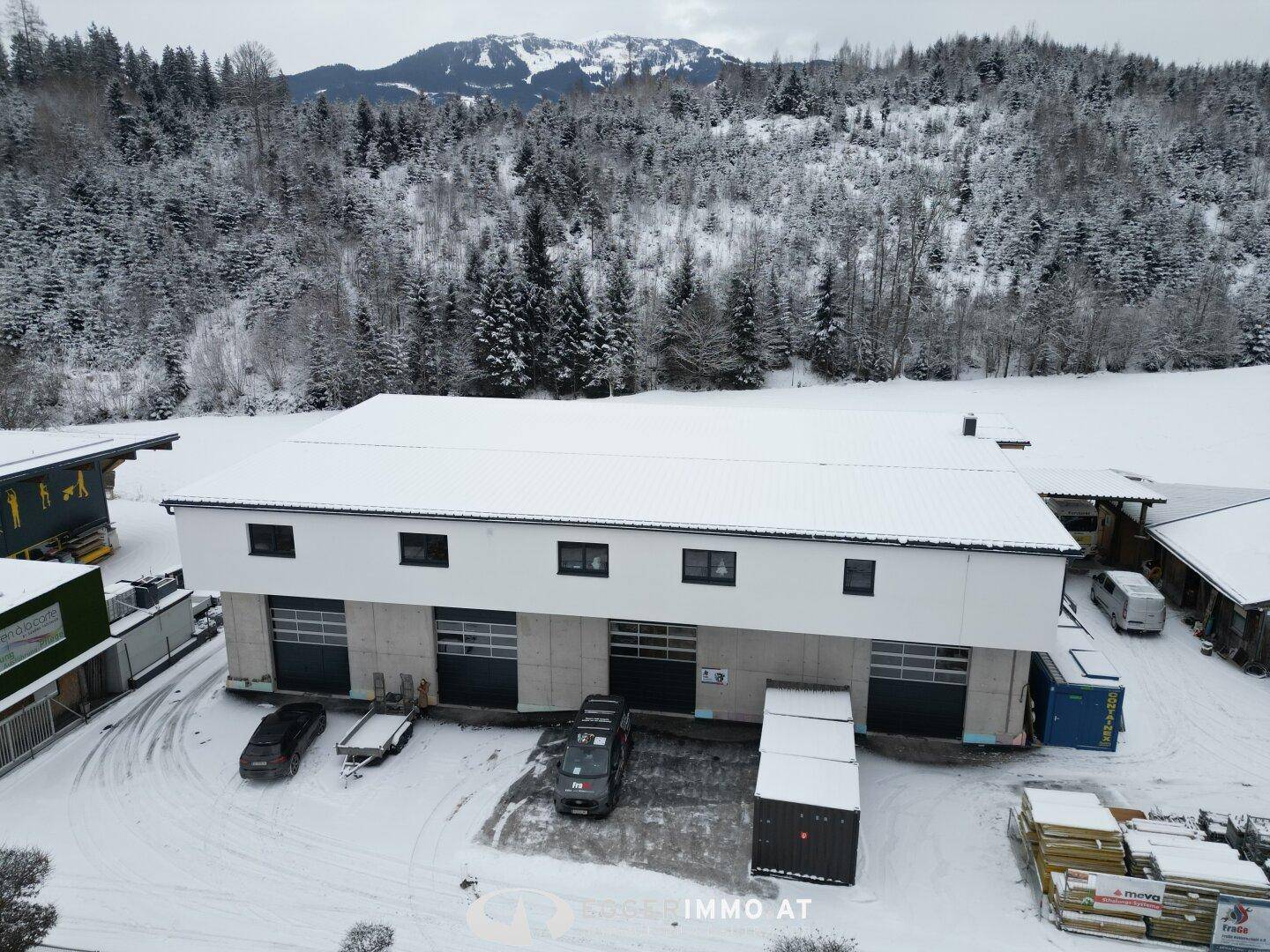 Nahaufnahme aus der Luft des Gewerbegebäudes im Winter, mit verschneitem Gelände und Lieferwagen vor den Garagentoren.