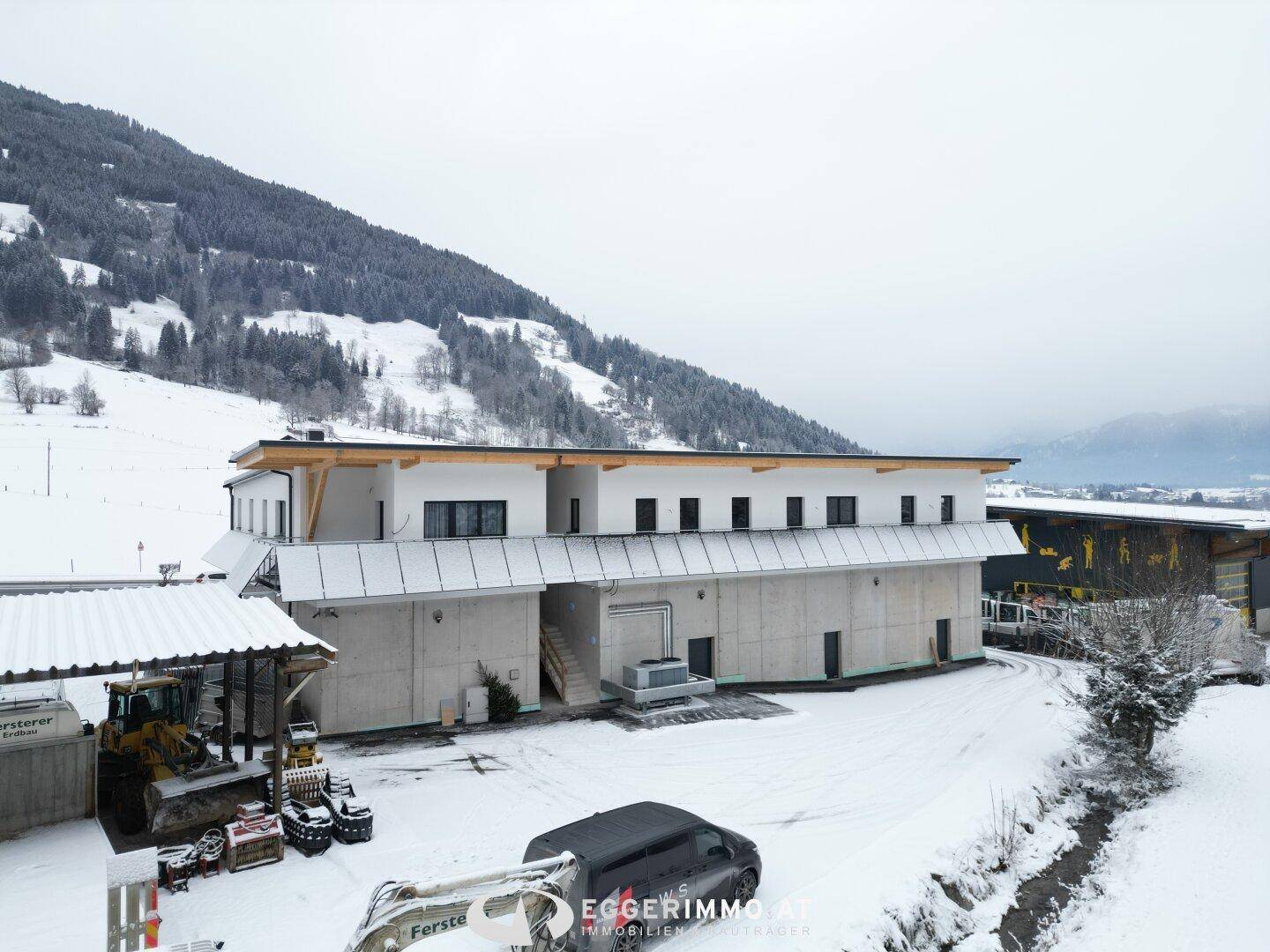 Seitenansicht des modernen Gebäudes im Winter, mit verschneiten Hängen und Bergen im Hintergrund, die die ländliche Umgebung zeigen.