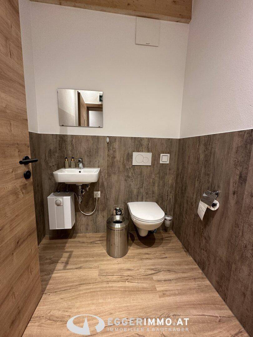 Modernes WC mit Waschbecken, Wand-WC und Holzdekor-Wandverkleidung, ausgestattet mit einem kleinen Boiler.