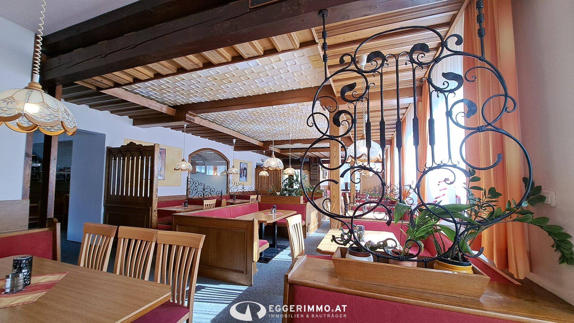 Rustikaler Restaurantbereich mit Holzbalken, roten Sitzbänken und schmiedeeisernen Dekorationen.