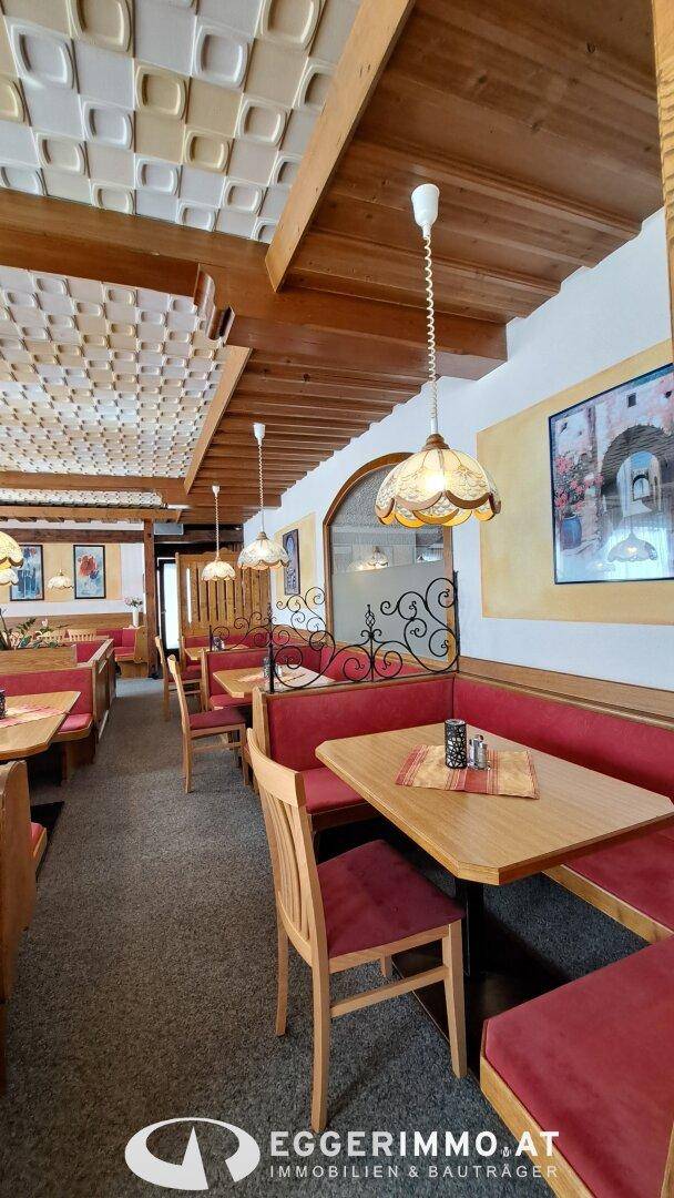 Langer Restaurantbereich mit Holztischen, roten Sitzbänken und traditionellen Deckenleuchten.