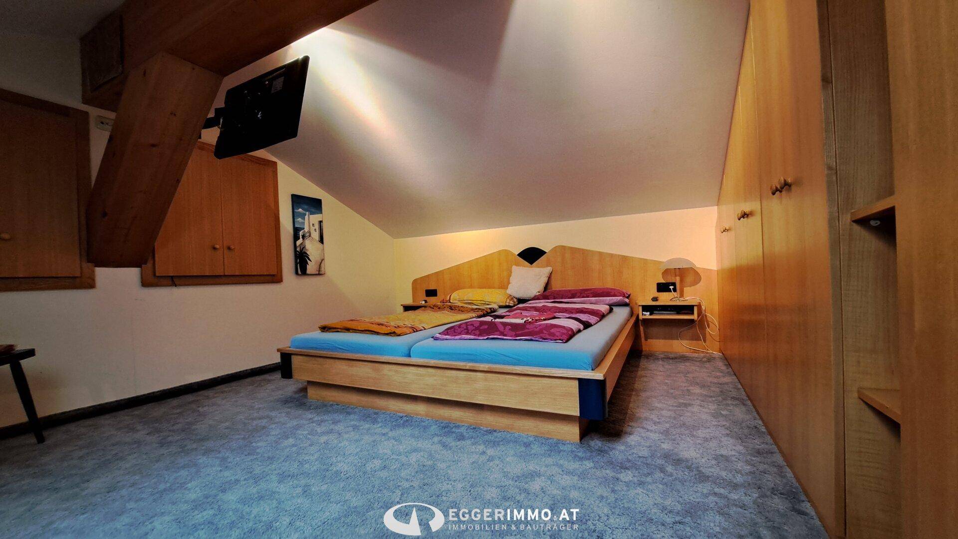 Gemütliches Schlafzimmer im Dachgeschoss mit Holzbett, Einbauschränken und schräger Decke.