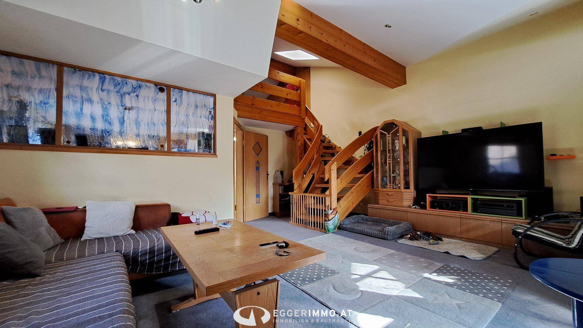 Wohnzimmer mit Holztreppe, Holzbalken und großem Fernseher, offen gestaltet.