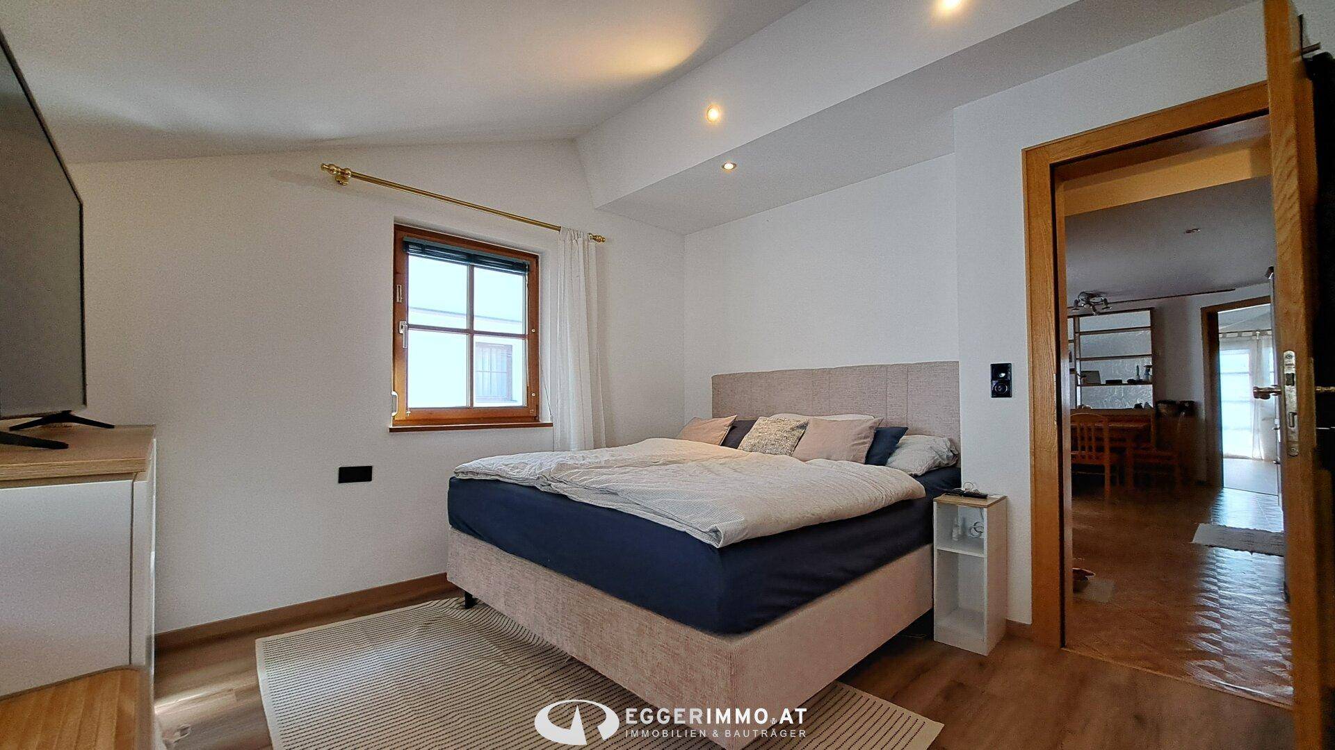 Helles Schlafzimmer mit Doppelbett, weiß gestrichenen Wänden und Holzboden.