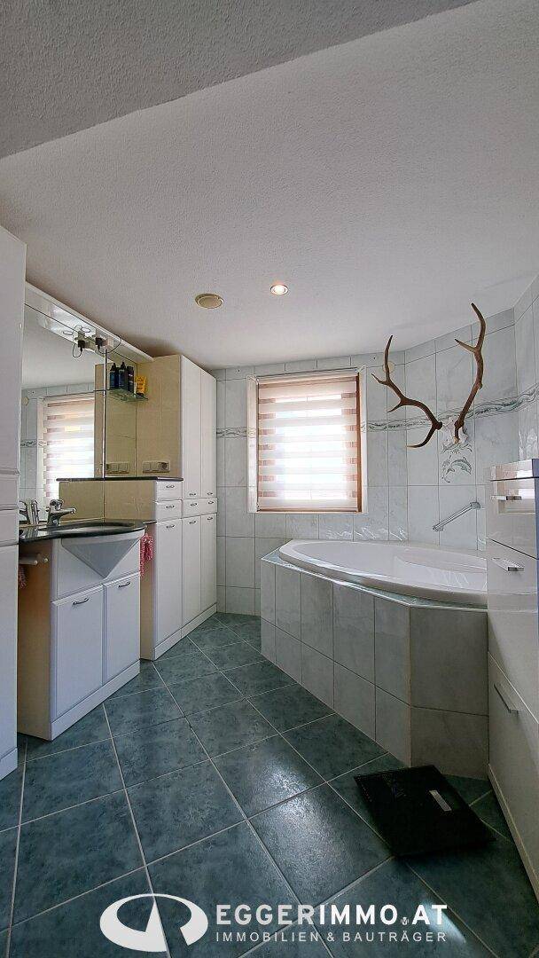 Badezimmer mit Eckbadewanne, Fliesenboden und Fenster, dekoriert mit Hirschgeweih.