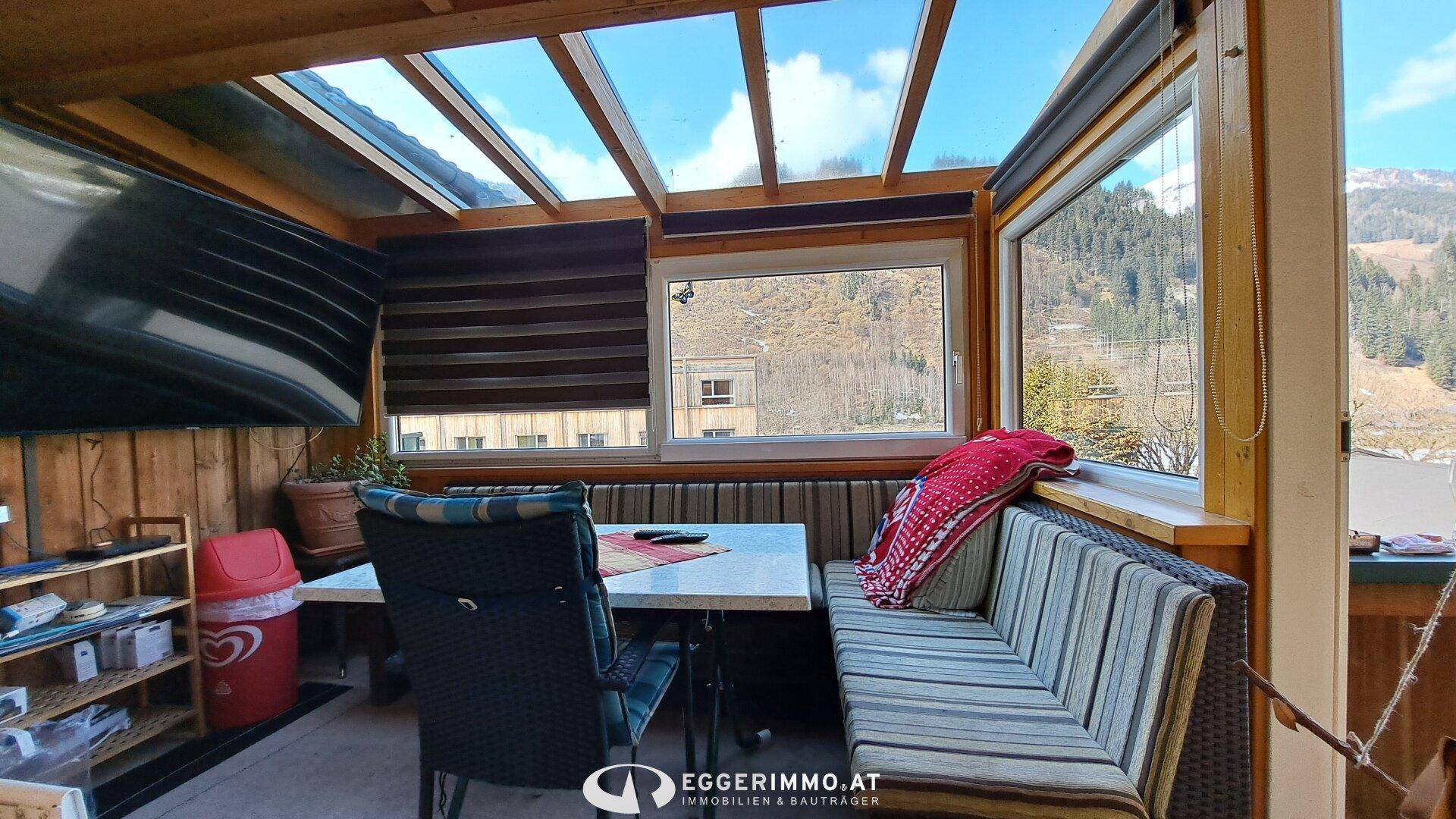 Heller Wintergarten mit Sitzgelegenheiten, Glasdach und Blick auf die umliegende Berglandschaft.