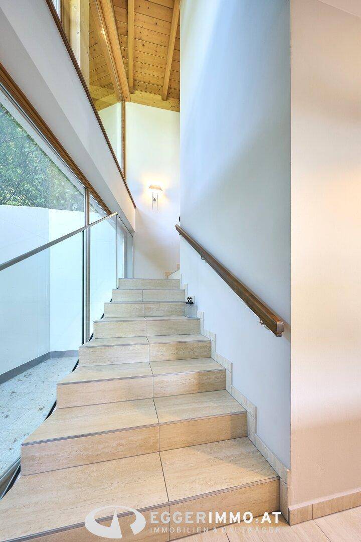 Elegante Treppe mit Glasgeländer und gefliesten Stufen, die zu den oberen Etagen führt.