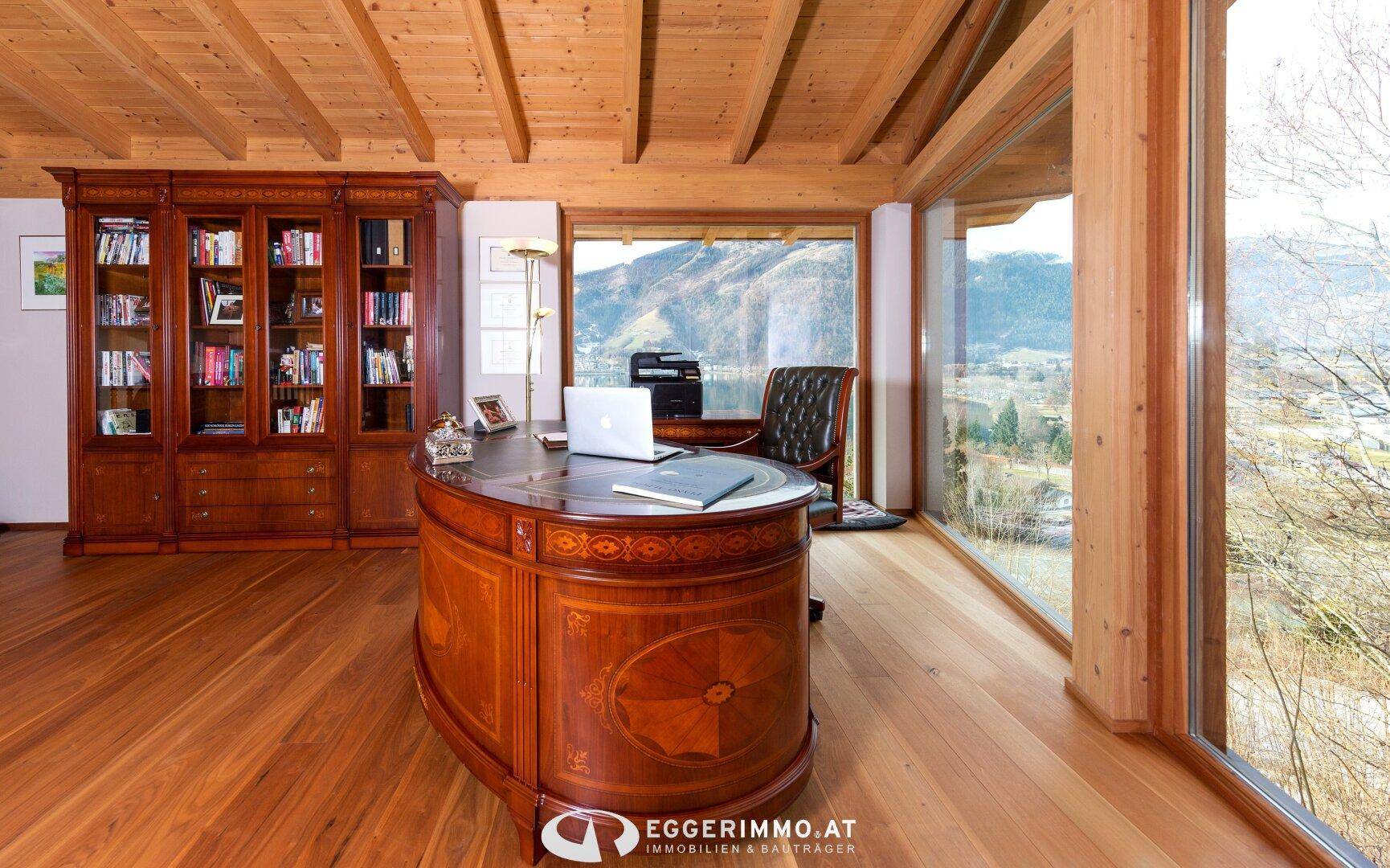 Elegantes Büro mit großem Holzschreibtisch, Bücherregal und Panoramafenstern mit weitem Ausblick.