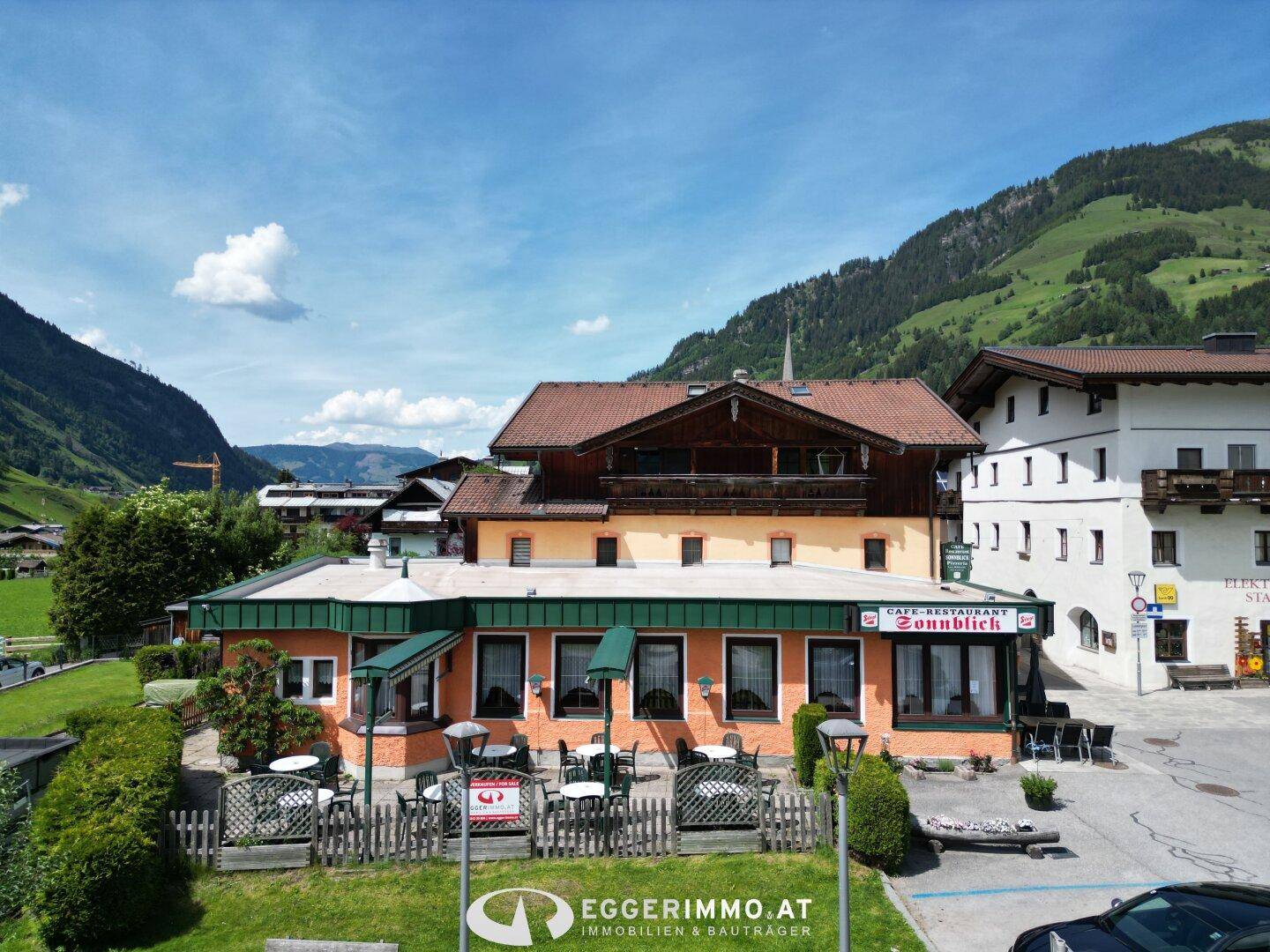 Ansicht des Restaurants mit Außenterrasse und Sonnenschirmen vor einer malerischen Bergkulisse.