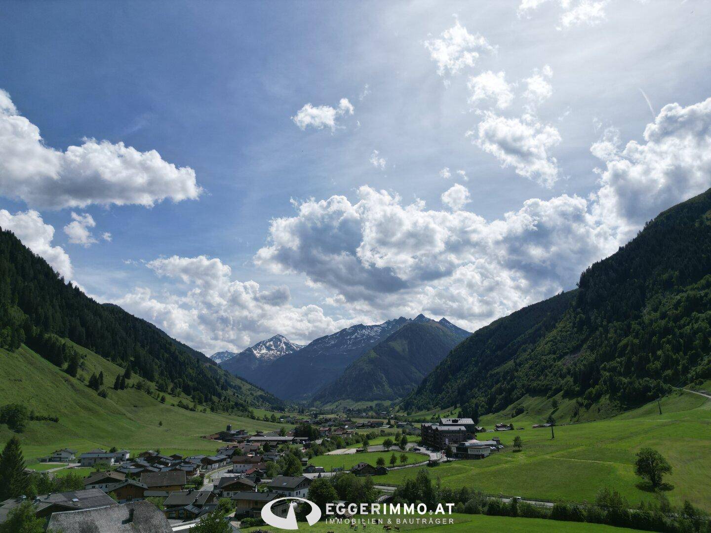 Atemberaubender Panoramablick auf ein weites Alpental mit schneebedeckten Berggipfeln in der Ferne.