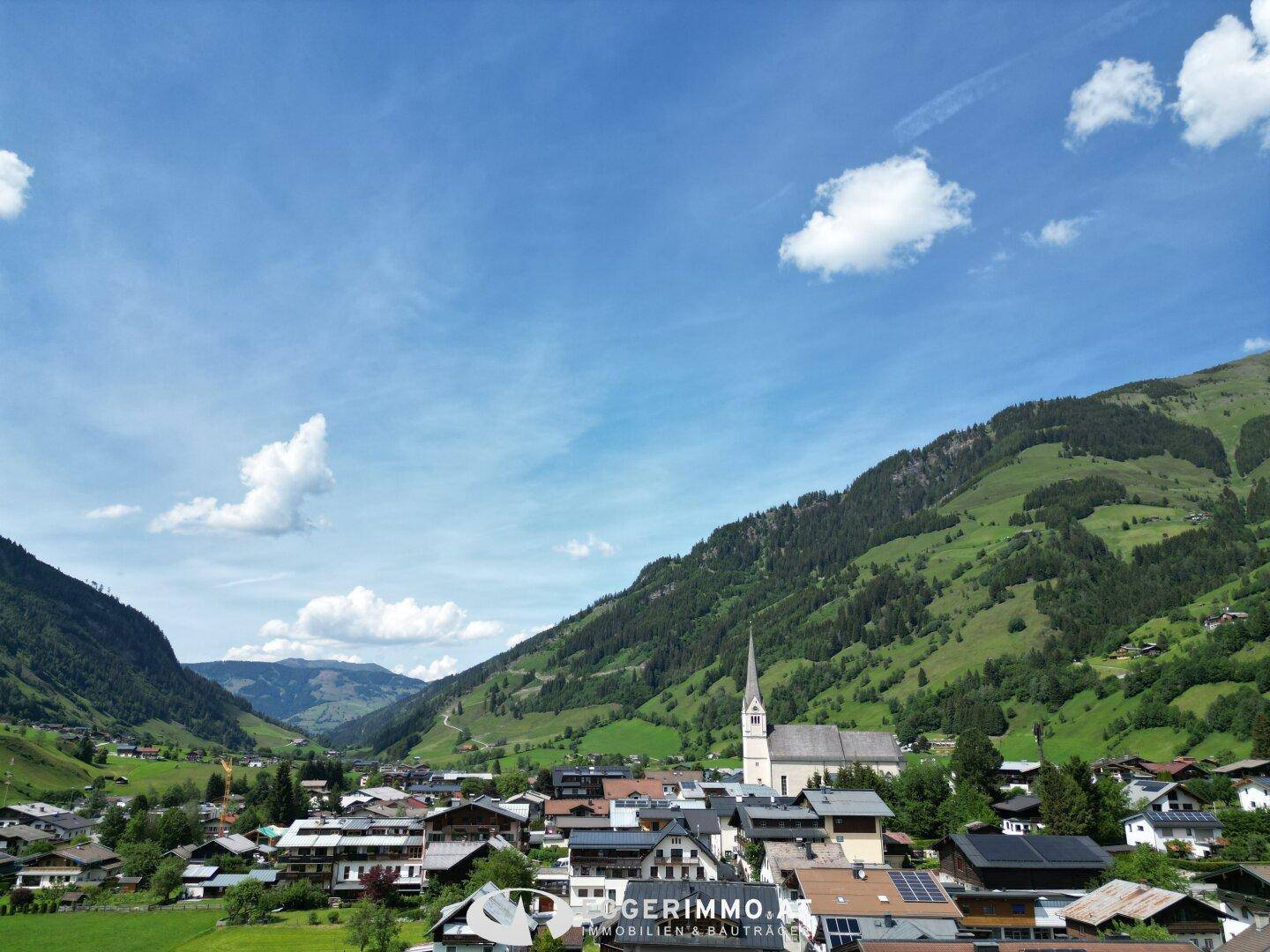 Weitläufiger Blick über ein idyllisches alpines Tal mit einem Dorf und einer Kirche.