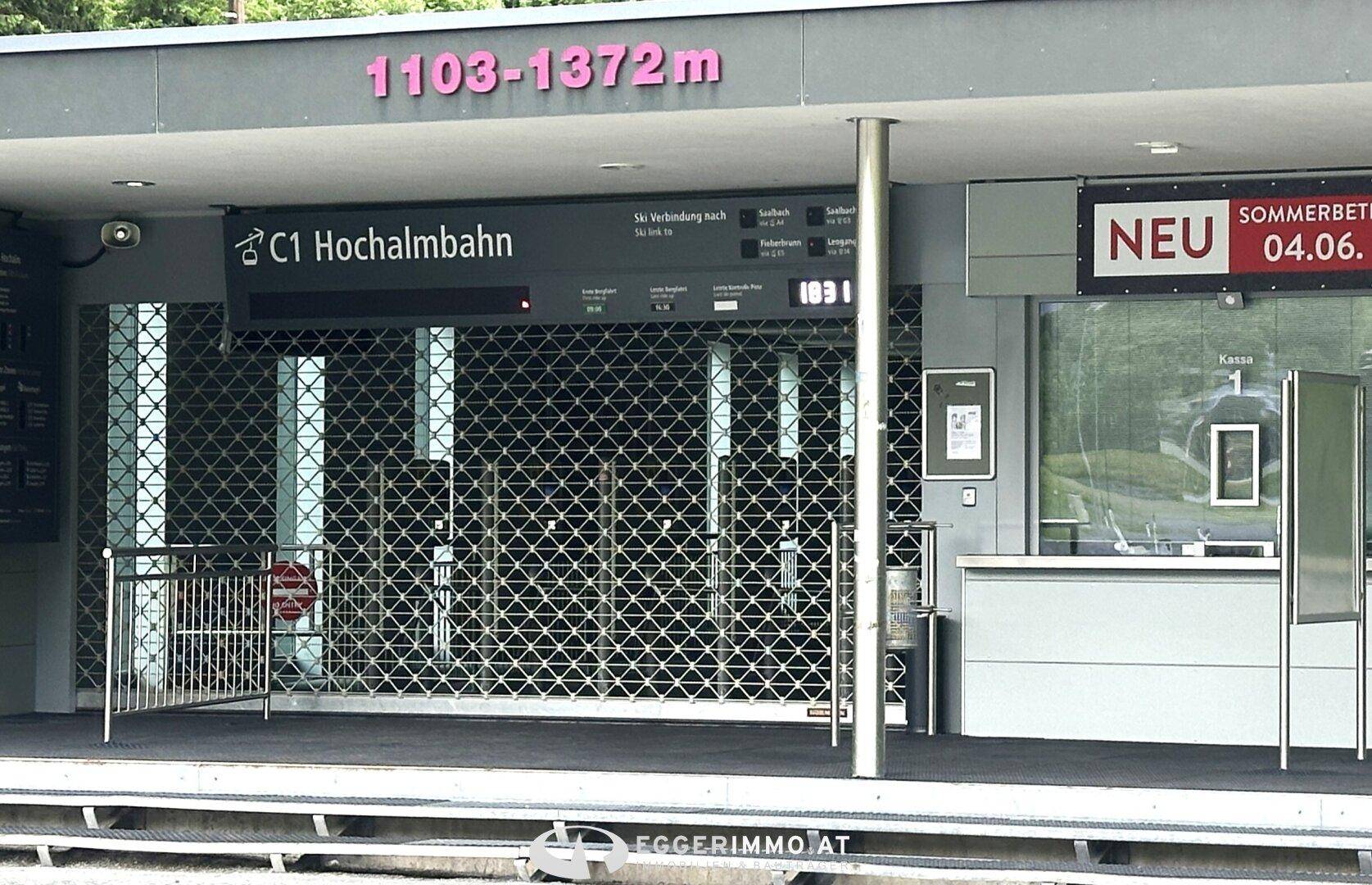 Eingangsbereich einer geschlossenen Seilbahnstation mit Metallgitter und Informationsschildern.