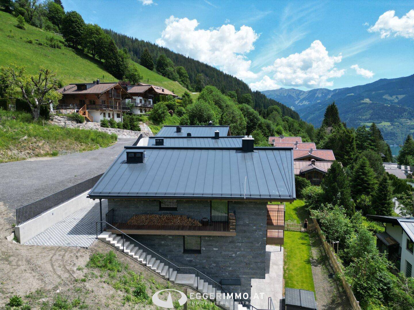 Modernes Chalet mit Steinfassade, Holzdetails und Balkonen in sonniger Hanglage mit Bergblick.