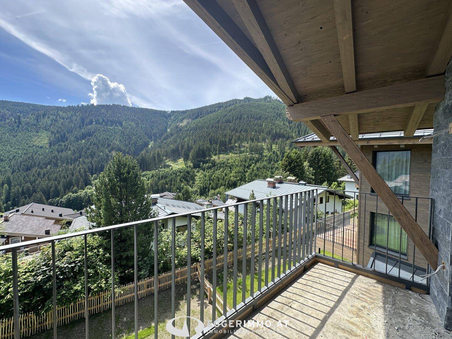 Geräumiger Balkon mit Holzdecke und Blick auf die bewaldeten Berghänge unter blauem Himmel.