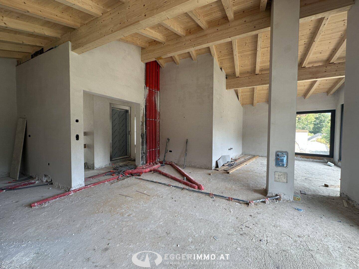 Innenraum im Rohbau mit sichtbaren Holzbalken und Installationen, bereit für den finalen Ausbau.