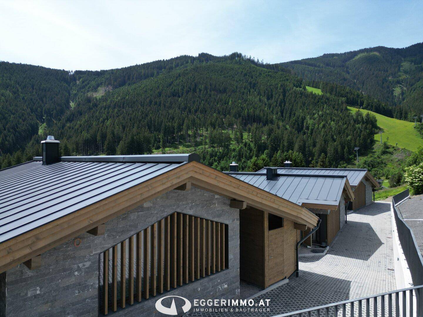 Dächer von modernen Chalets mit Holzverkleidung und Blick auf bewaldete Berge.
